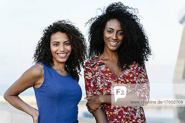 Lächelnde junge Frauen in Freizeitkleidung stehen gegen den Himmel