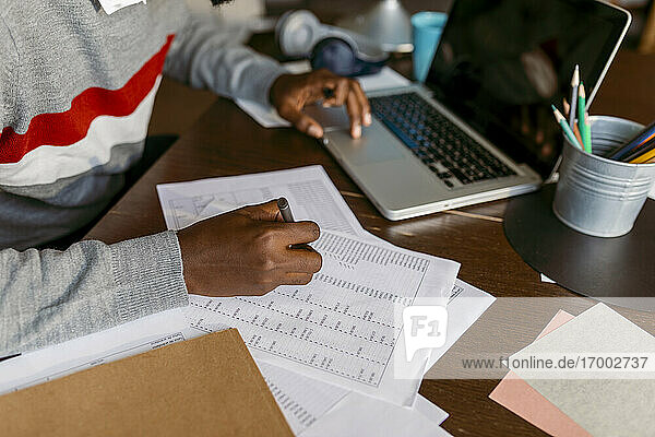 Männlicher Finanzberater  der zu Hause am Laptop eine Strichliste auf Papier erstellt