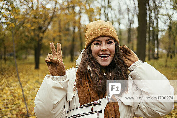 Schöne Frau macht Friedenszeichen  während sie im Herbst im Park steht