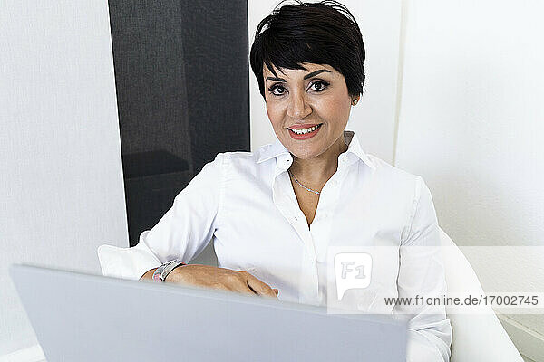 Portrait of businesswoman smiling at camera while sitting with laptop