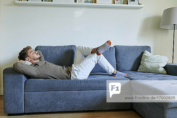 Man resting on sofa with hands behind head in living room at home