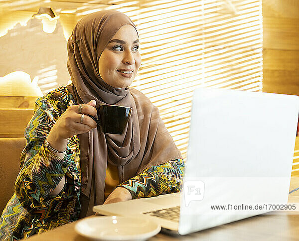 Frau trägt Hijab und trinkt Kaffee  während sie im Cafe sitzt