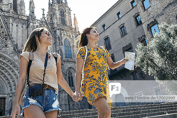 Freundinnen halten sich an den Händen  während sie gegen den Platz der Kathedrale von Barcelona in Barcelona  Katalonien  Spanien  laufen