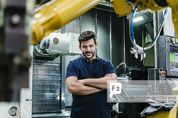 Male manual worker with arms crossed smiling while standing in factory