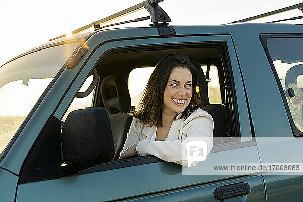 Happy beautiful woman looking out of car window during road trip
