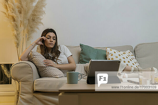 Young woman with digital tablet relaxing on sofa at home