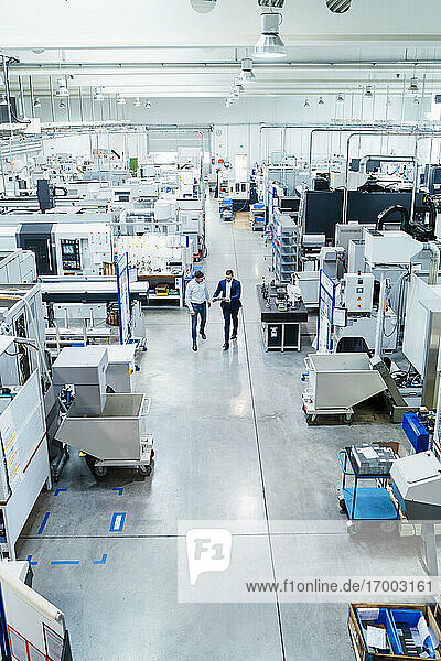 Männliche Mitarbeiter gehen in einer Fabrik  umgeben von Produktionsanlagen