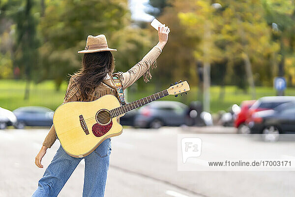 Junge Frau mit Gitarre winkt dem Taxi auf der Straße zu