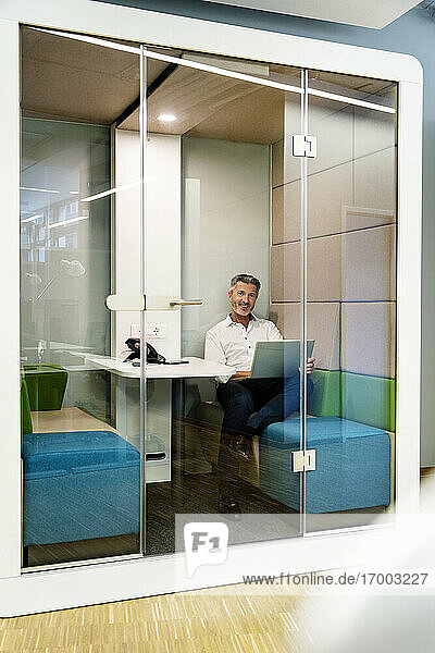 Geschäftsmann  der einen Laptop benutzt  während er in einer Kabine im Büro sitzt