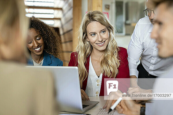 Lächelnde Frau  die einen Kollegen ansieht  während sie in einer Besprechung im Büro sitzt