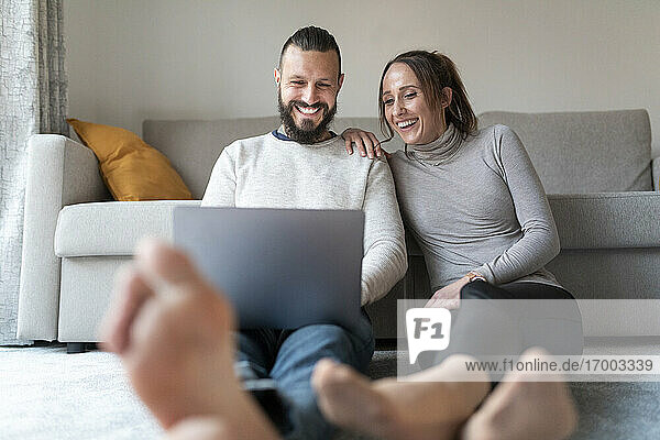 Paar lacht  während es im Wohnzimmer einen Film auf dem Laptop ansieht