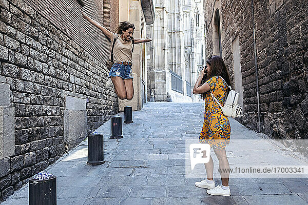 Frau fotografiert einen Freund  der auf dem Fußweg im Gotischen Viertel in Barcelona  Katalonien  Spanien  springt