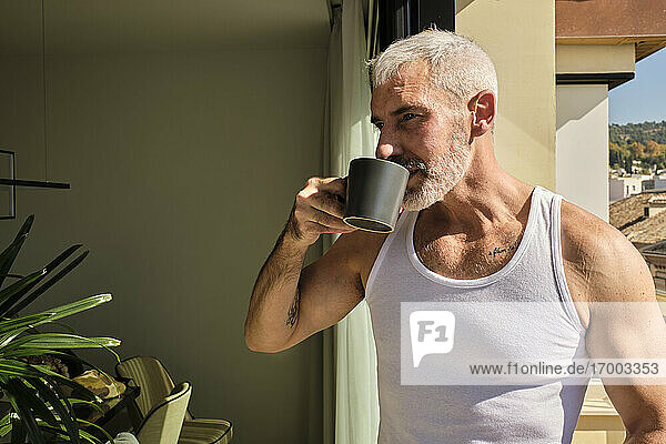 Mature man drinking morning coffee in living room on sunny day