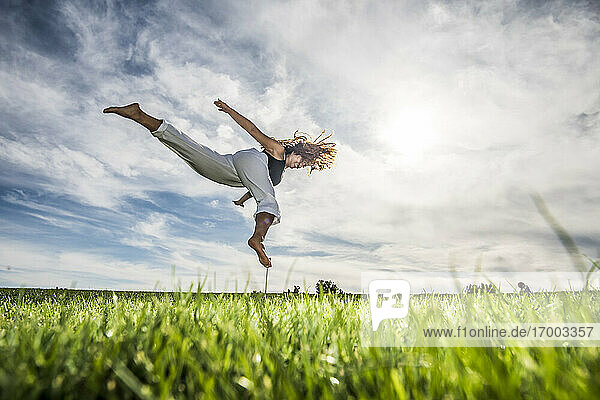 Weibliche Athletin springt in der Luft über Gras im Park gegen bewölkten Himmel