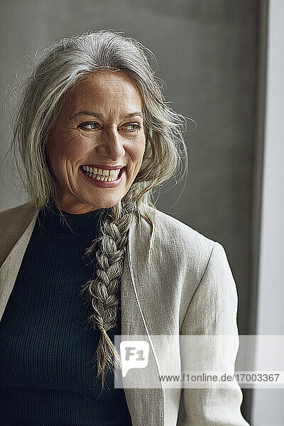 Lächelnde Unternehmerin  die in ihrem Büro zu Hause gegen eine graue Wand blickt