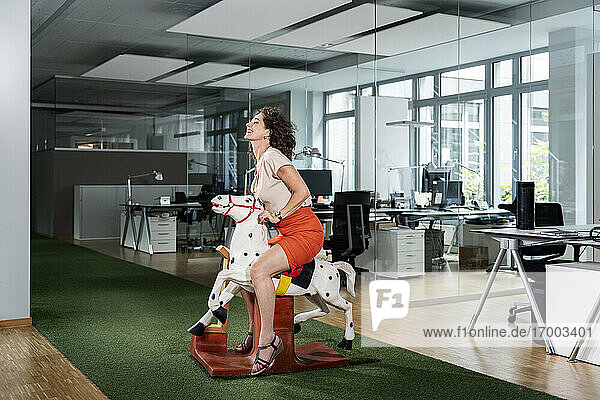 Smiling businesswoman sitting on rocking horse at office