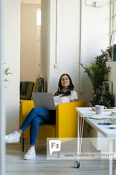 Geschäftsfrau mit Laptop auf einem Sessel im Büro sitzend