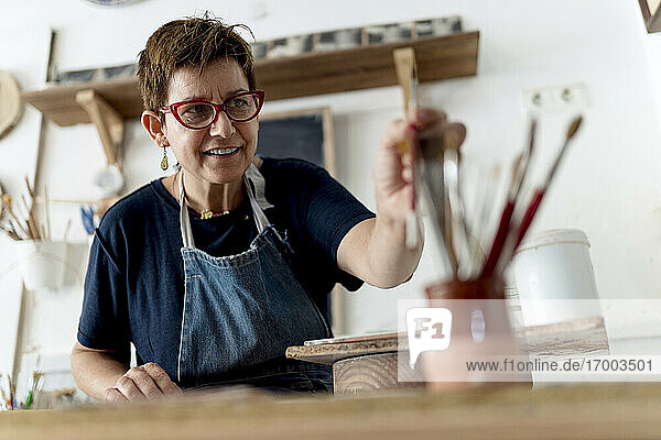 Lächelnde Künstlerin bei der Wahl des Pinsels in der Keramikwerkstatt