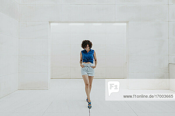 Stylish woman with curly hair walking on tiled floor against wall