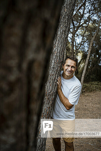 Lächelnder Mann an einem Baumstamm im Wald im Urlaub