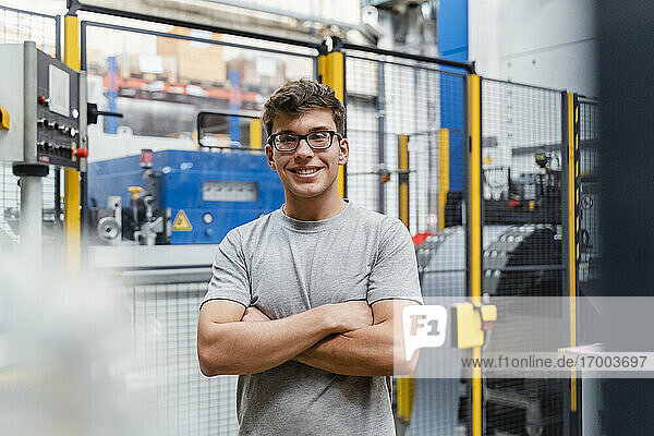 Lächelnder männlicher Ingenieur mit verschränkten Armen in beleuchteter Industrie