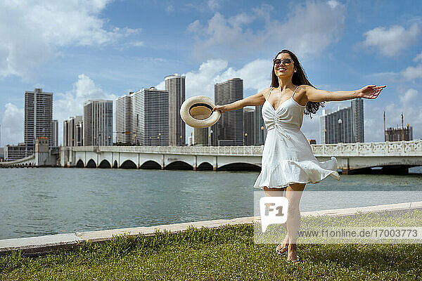 Glückliche junge Frau  die sich im Gras an der Bucht vor dem Himmel dreht