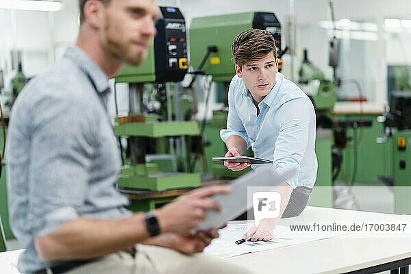 Male engineer holding digital tablet with entrepreneur looking away while having meeting in factory