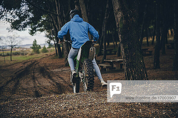 Männlicher jugendlicher Motorradfahrer auf einem Geländemotorrad im Wald