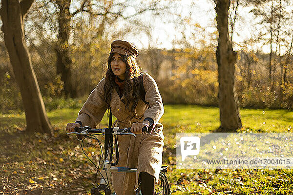 Modische Frau sitzt auf einem Fahrrad in einem öffentlichen Park