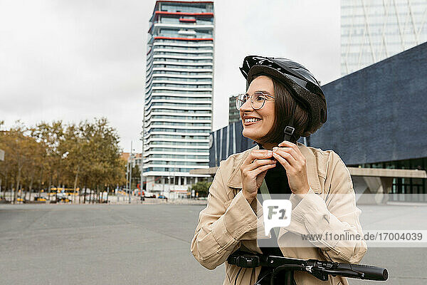 Lächelnde Frau mit Fahrradhelm auf der Straße in der Stadt