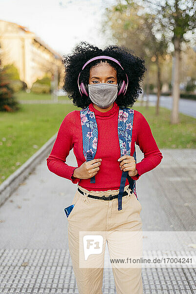 Frau mit Schutzmaske und Kopfhörern  die einen Rucksack trägt  während sie auf einem Fußweg steht