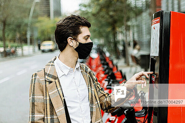 Young man in face mask renting bicycle in city