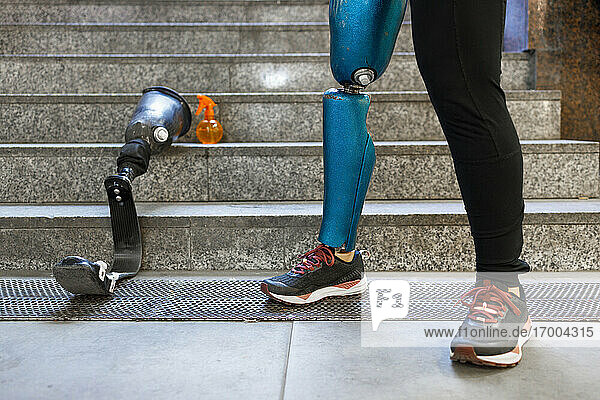 Young sportswoman with prosthetic leg standing by artificial limb on steps
