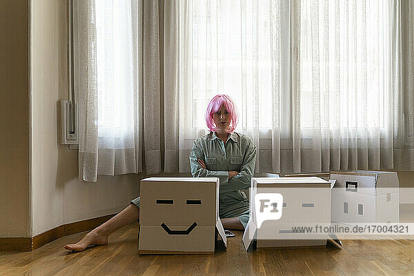 Ernste junge Frau mit rosa Perücke sitzt auf dem Boden mit Smiley und Stirnrunzeln Gesicht Karton
