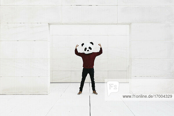 Mann mit Pandamaske  der Muskeln anspannt  während er an der Tür vor einer weißen Wand steht
