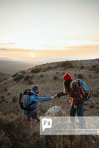Freundin hält Hand von Freund Klettern felsigen Berg gegen den Himmel bei Sonnenuntergang