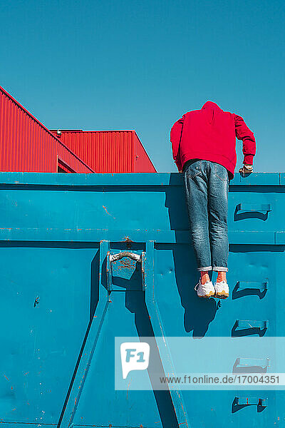 Young man pushing up  looking into blue container  rear view