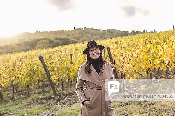 Lächelnde Unternehmerin mit Händen in den Taschen in einem Weinberg im Herbst stehend