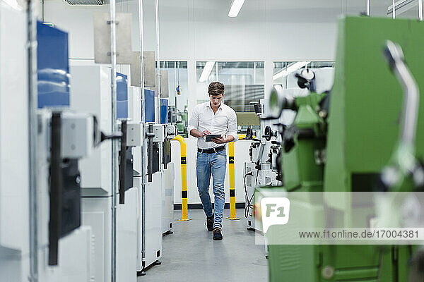 Male professional working on digital tablet while walking in industry