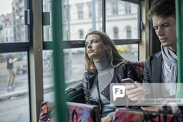 Nachdenkliche Frau  die mit einem männlichen Kollegen im Bus sitzt und ein Smartphone benutzt