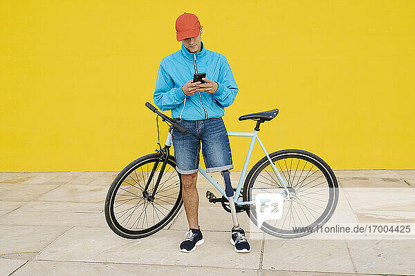 Man with artificial limb and foot standing by bicycle against yellow wall
