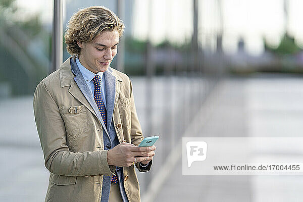 Young businessman using mobile phone while standing outdoors
