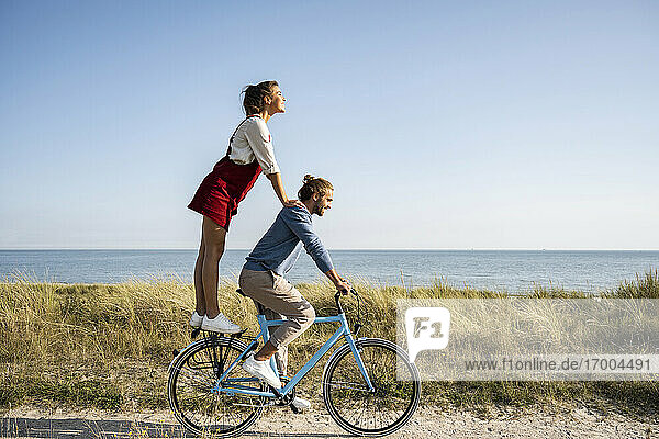 Girlfriend enjoying ride with man while standing on bicycle against clear sky