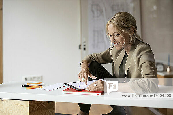 Lächelnde Geschäftsfrau  die ein digitales Tablet benutzt  während sie zu Hause sitzt