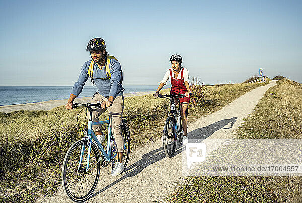 Girlfriend and boyfriend riding bicycles on sunny day against clear sky