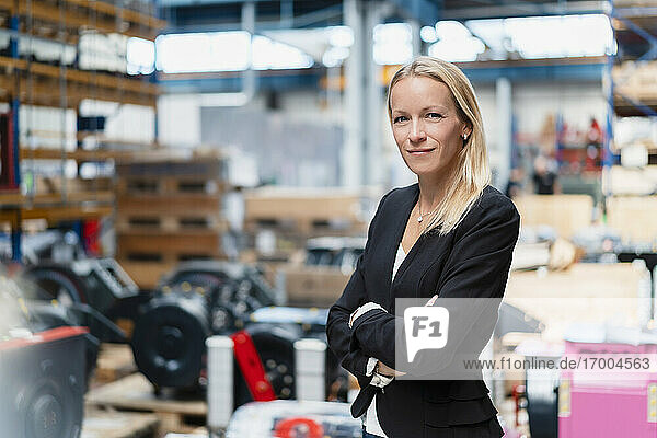 Confident businesswoman with arms crossed standing in factory