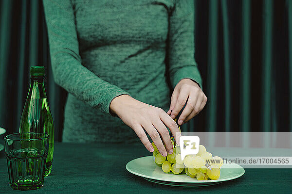 Midsection of woman with grapes  glass  bottle kept on table