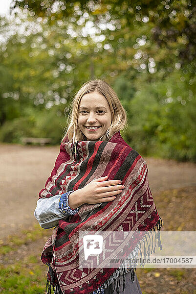 Lächelnde Frau in Schal eingewickelt im Herbst im Park
