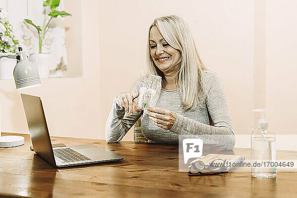 Lächelnde ältere Frau mit einer medizinischen Probe während einer Online-Konsultation zu Hause