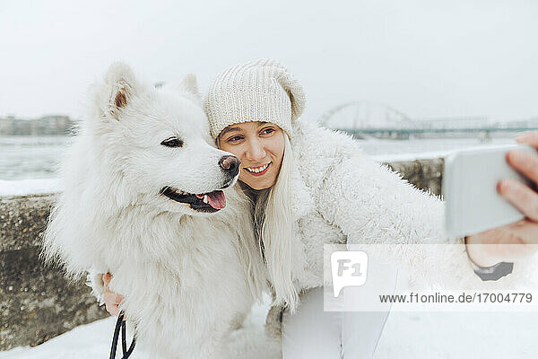 White dressed woman taking selfie with her white dog in winter